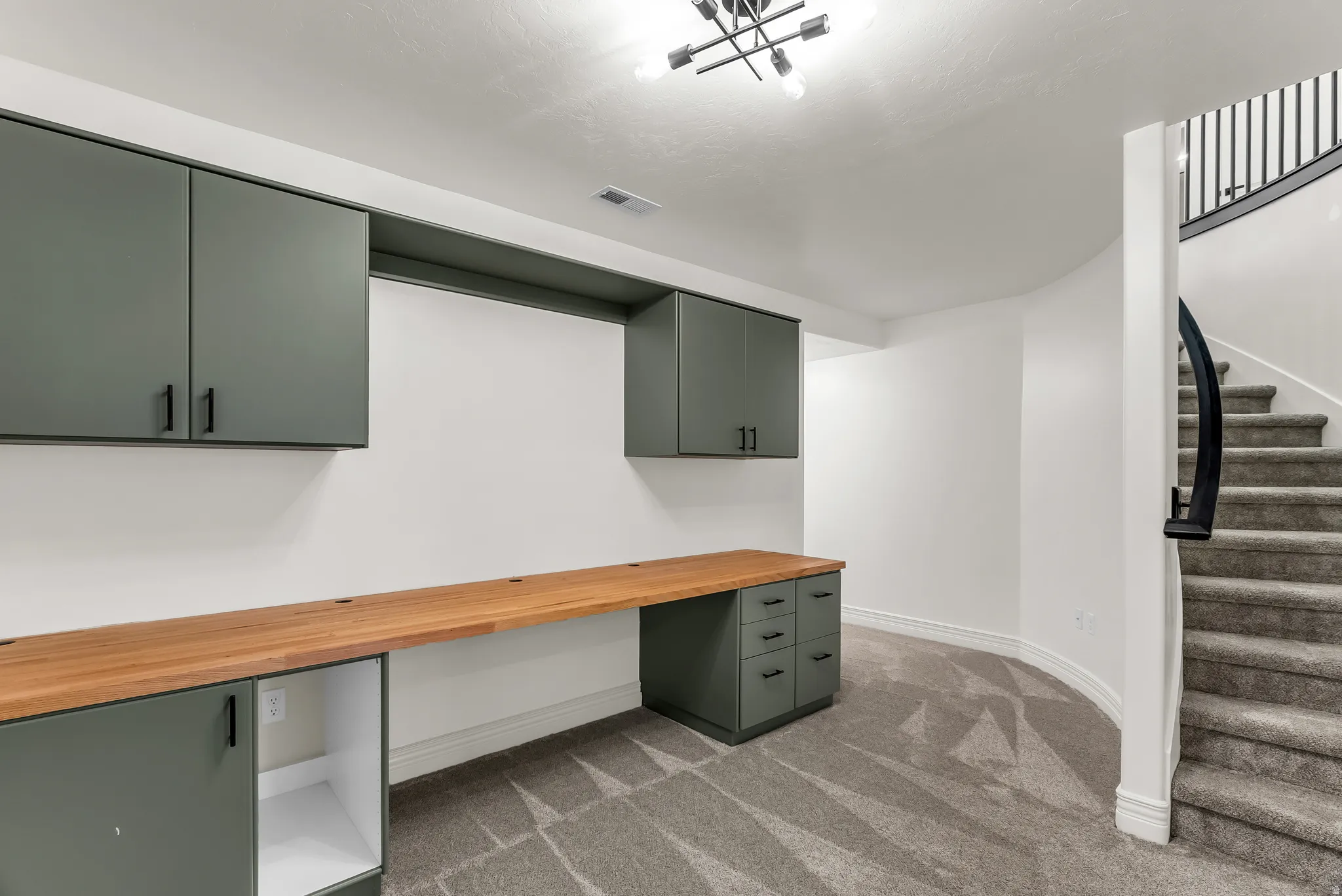 Built-in cabinetry with a wood-finish countertop, dark metal light fixture, and carpeted staircase with a dark metal railing