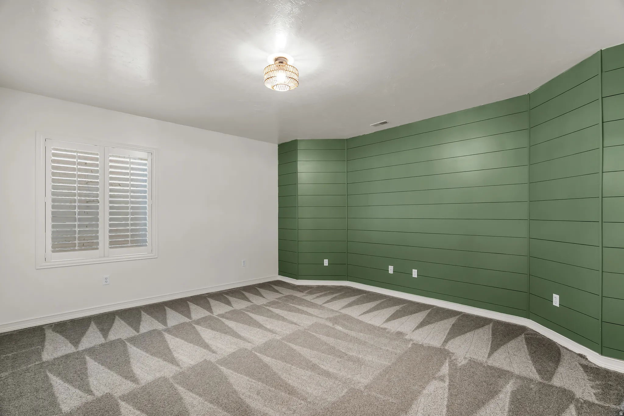 Patterned carpeting, window with plantation shutters, accent wall with horizontal paneling, and an attached flush-mount ceiling light