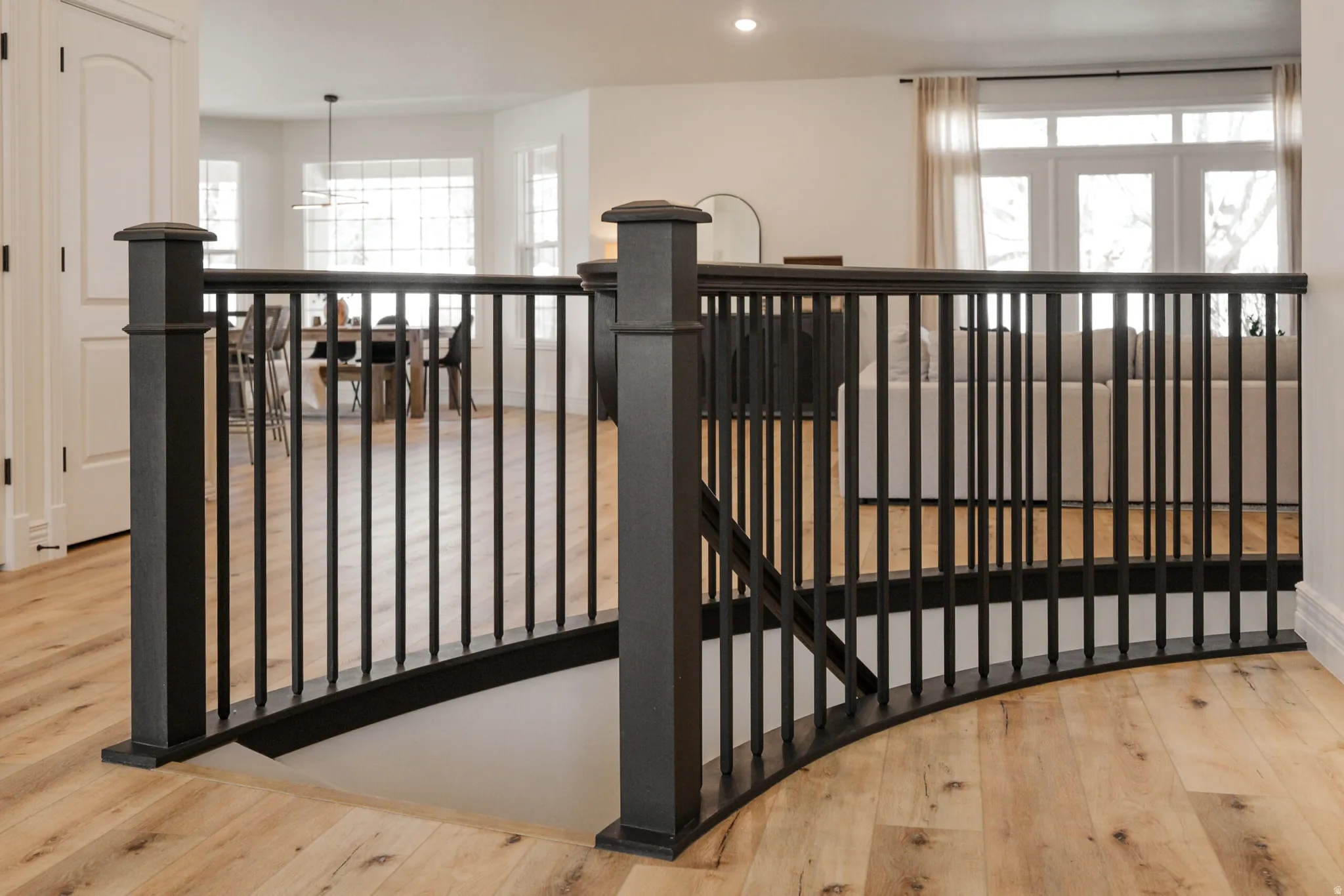 Curved open staircase with black newel posts and railings, wood-finish flooring, and white interior doors