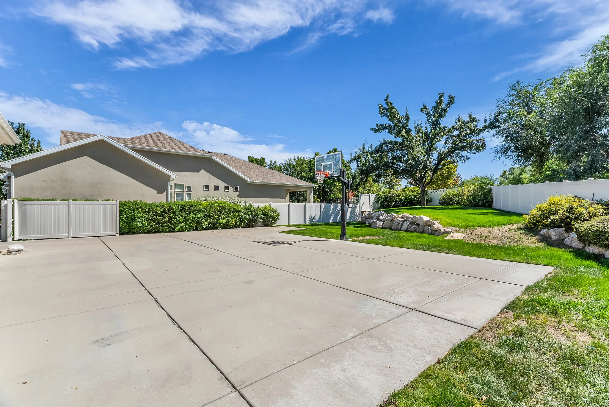 Expansive concrete driveway with a basketball hoop, complemented by a manicured lawn and privacy fencing