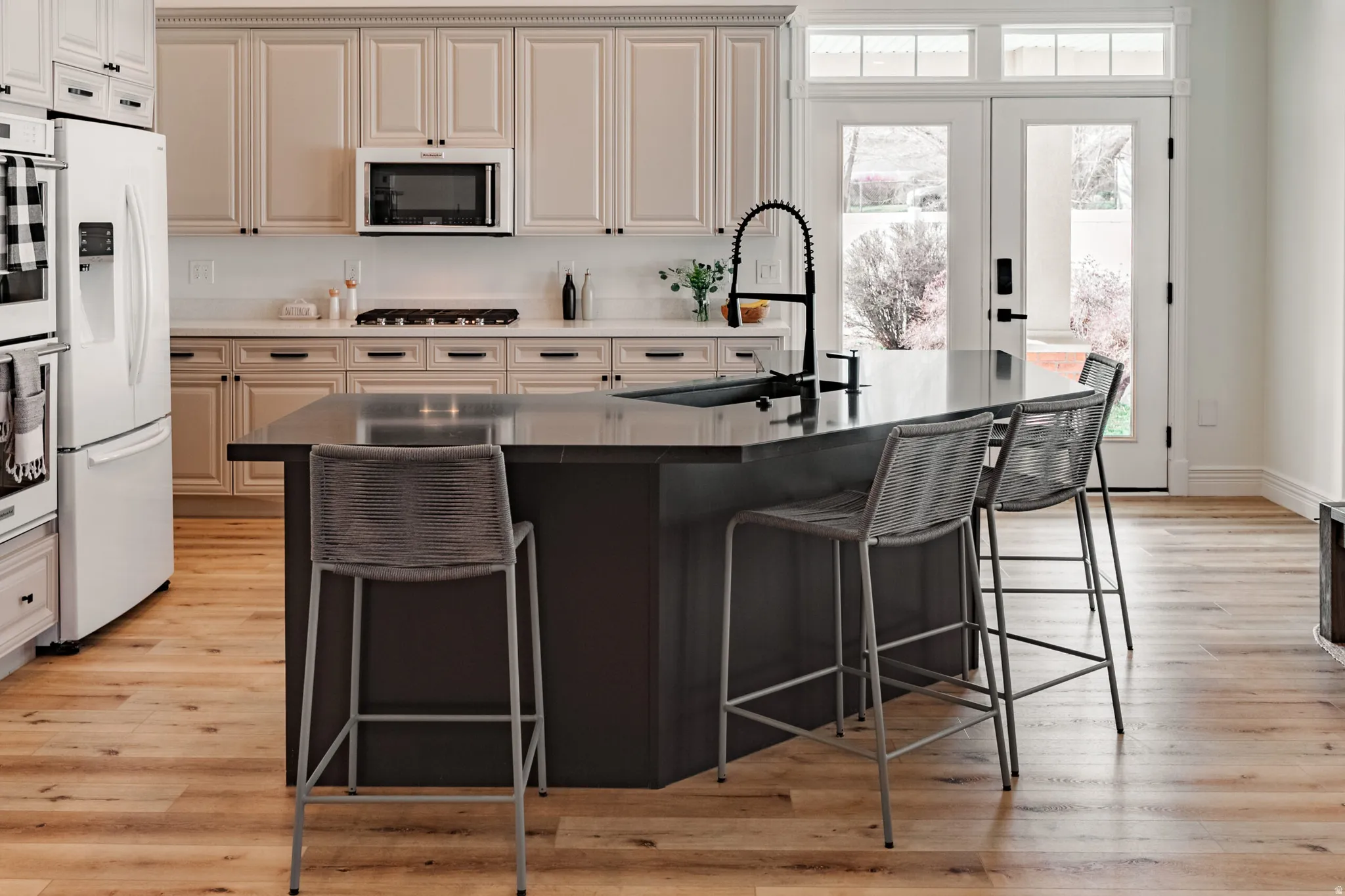 Wood-finish flooring, central island with an integrated sink, light-toned cabinetry, built-in stainless steel appliances, and double glass-paneled doors
