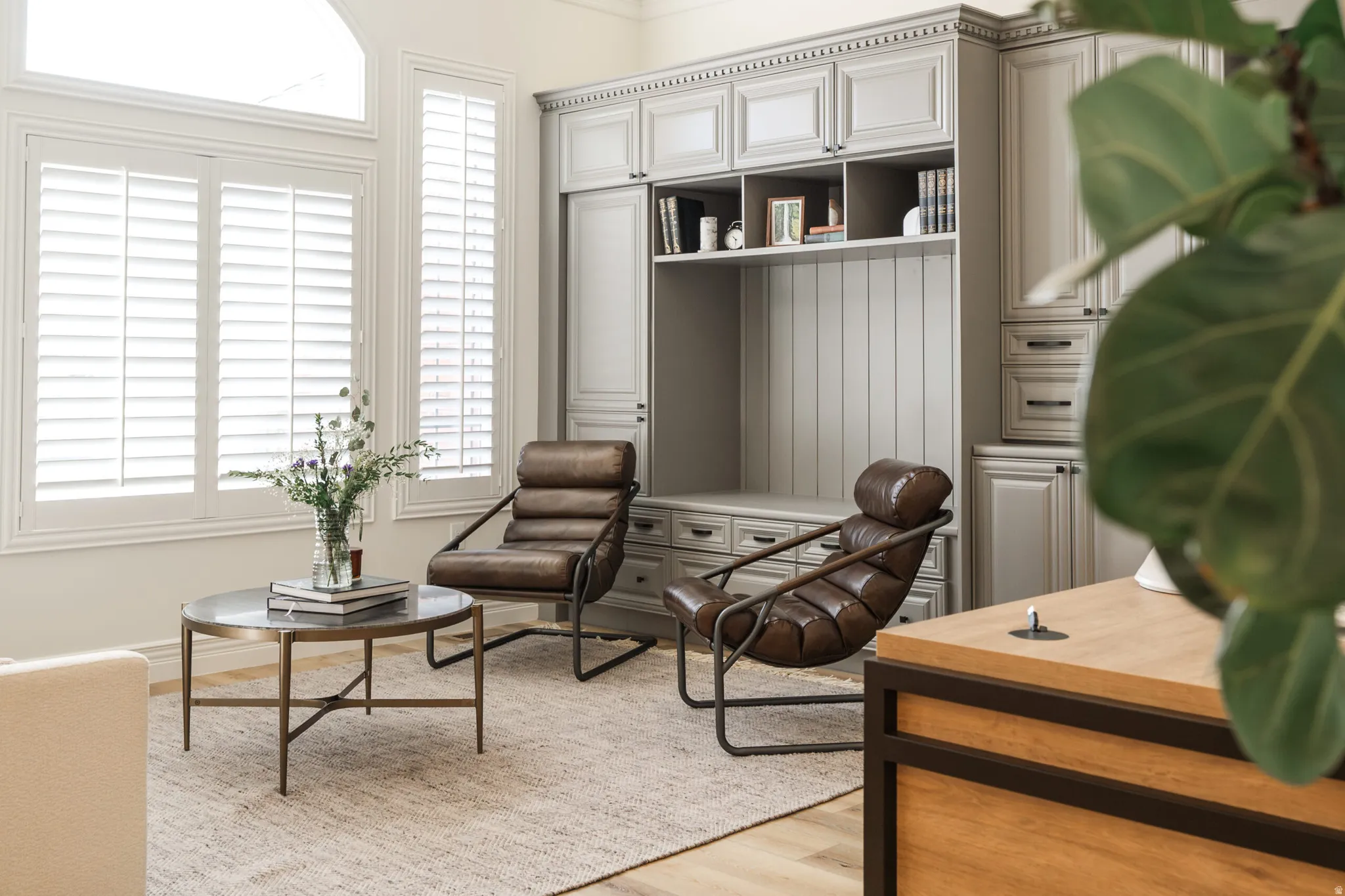Custom built-in cabinetry with beadboard detailing, window shutters, wood-finish flooring, crown molding, and a built-in shelving unit
