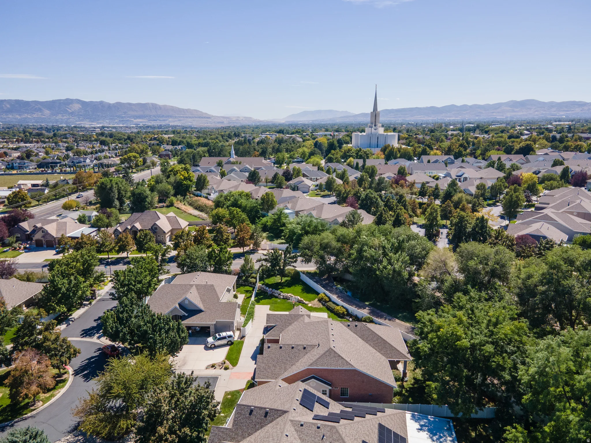 Residential neighborhood with mature trees, mountain backdrop, and distant architectural spire