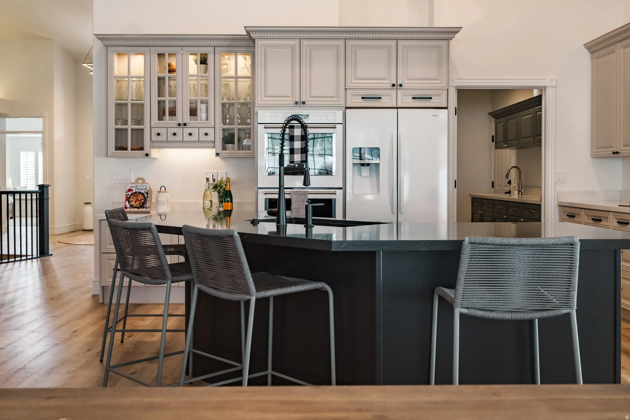 Central kitchen island with dark countertop, light-toned cabinetry with glass-front uppers, and stainless steel built-in appliances