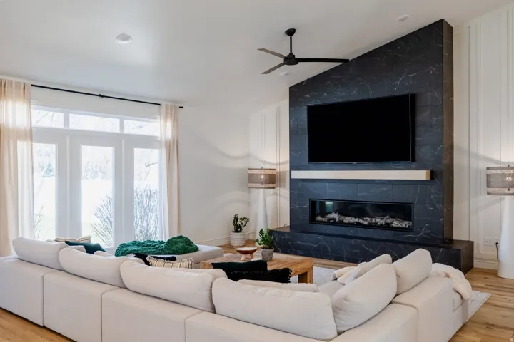 Spacious living area featuring a contemporary fireplace with a stone surround, a wood-finish mantel, and a ceiling fan
