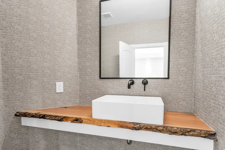 Live-edge wood vanity with a contemporary vessel sink, matte black wall-mounted faucet, and a rectangular mirror