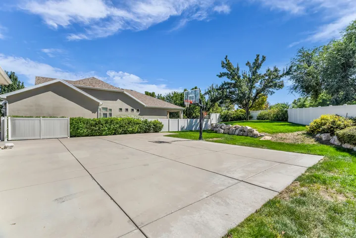 Expansive concrete driveway with a basketball hoop, complemented by a manicured lawn and privacy fencing
