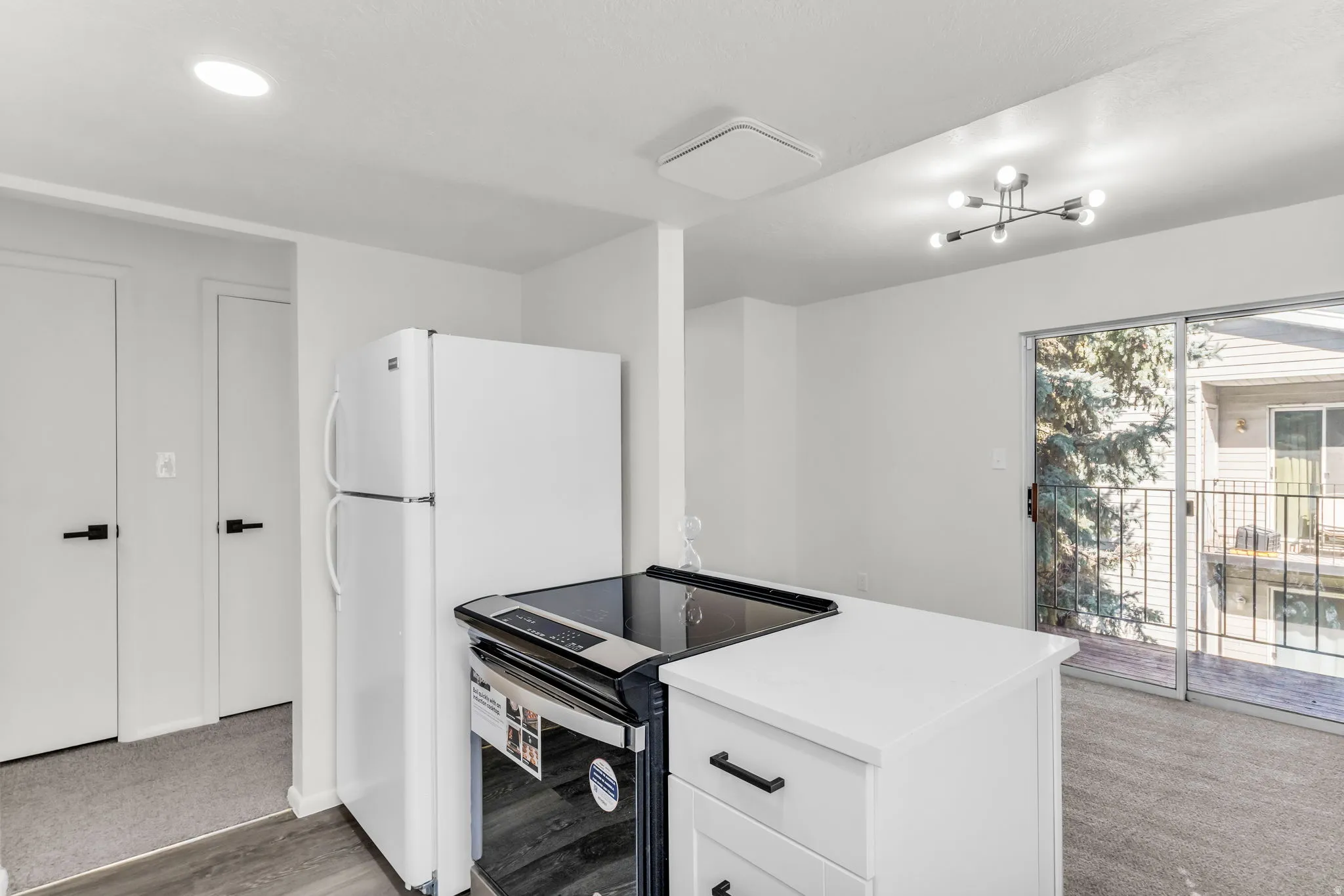 White kitchen cabinetry with matte black hardware, white refrigerator, and a sliding glass door to an exterior balcony
