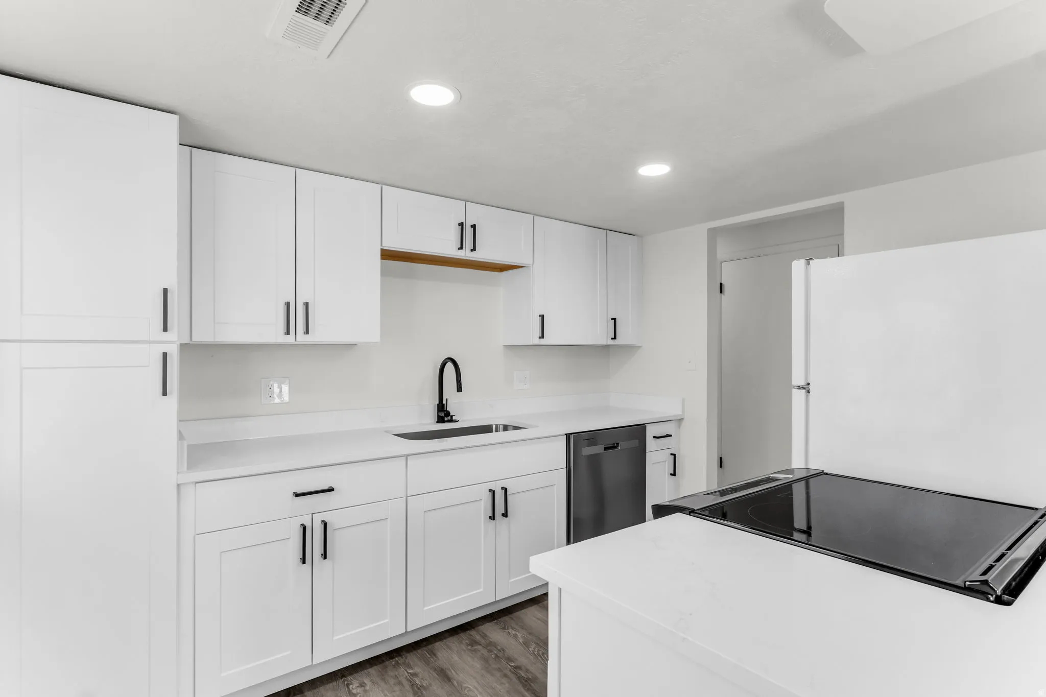 White shaker-style cabinetry with matte black hardware, solid surface countertops, undermount sink with a black gooseneck faucet, stainless steel dishwasher, and wood-finish flooring