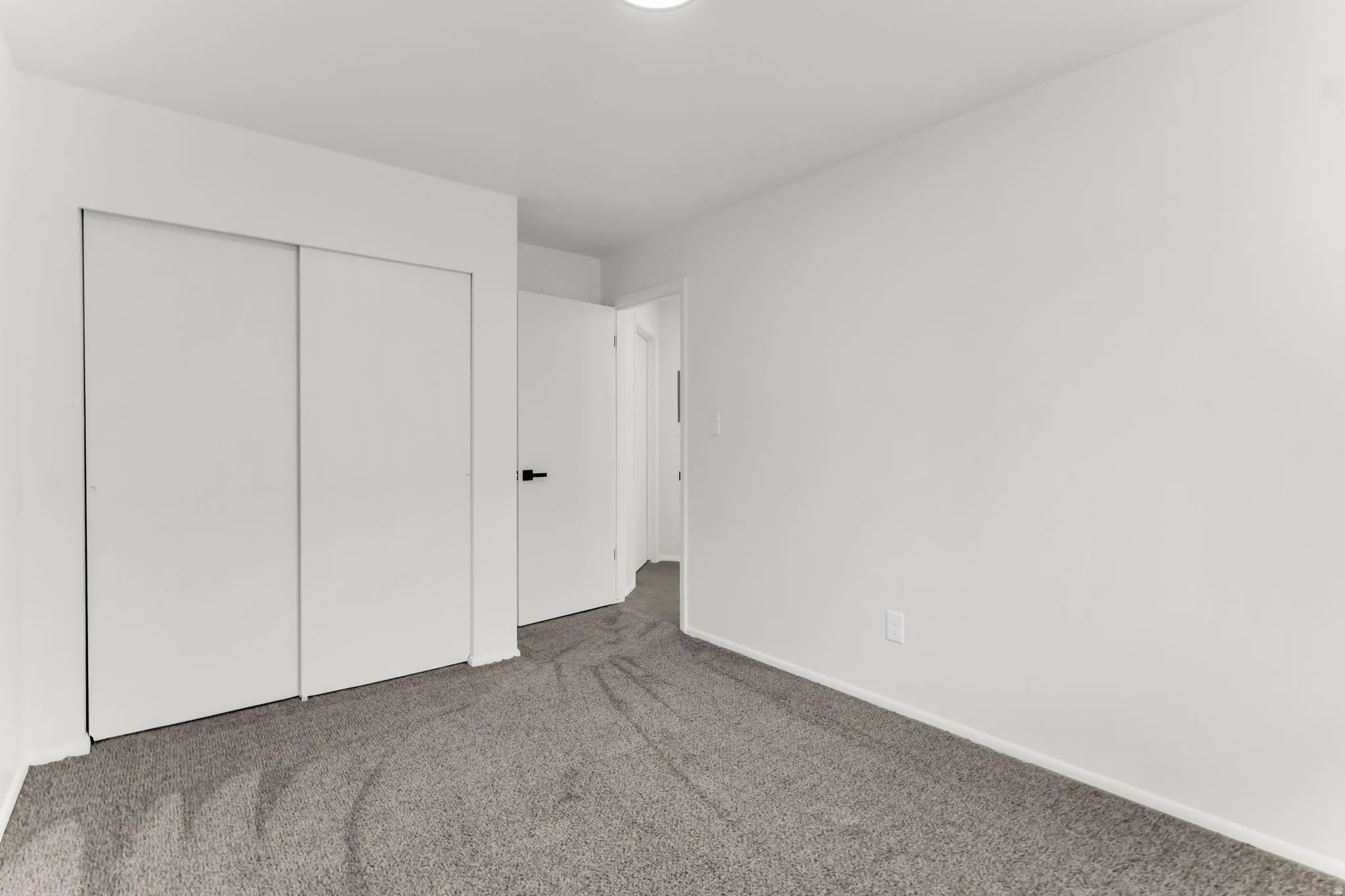 Neutral wall color, gray carpeting, white bi-fold closet doors, white interior door with black hardware, and overhead lighting