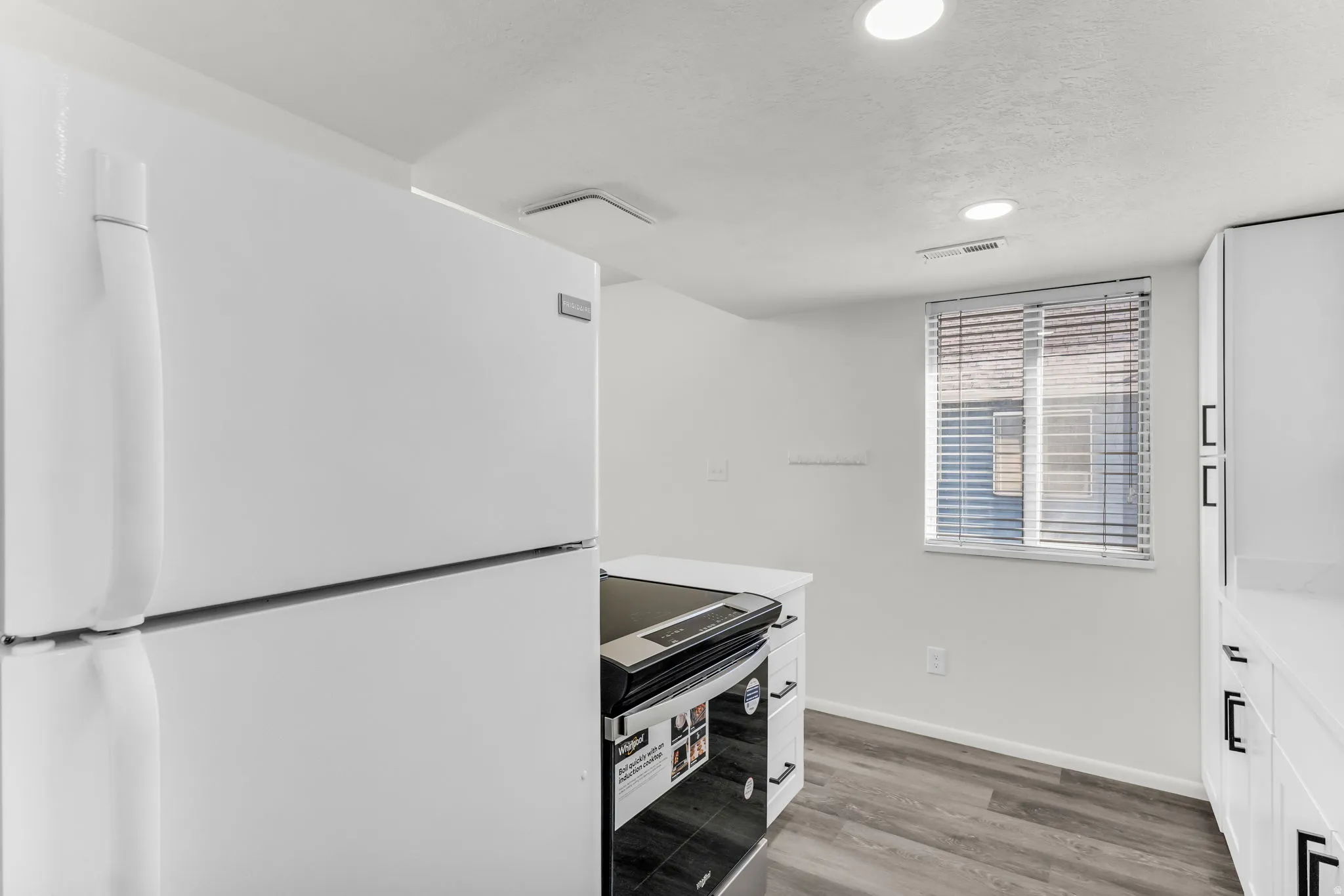 White refrigerator, white cabinetry, dark gray wood-finish flooring, white walls, and recessed lighting