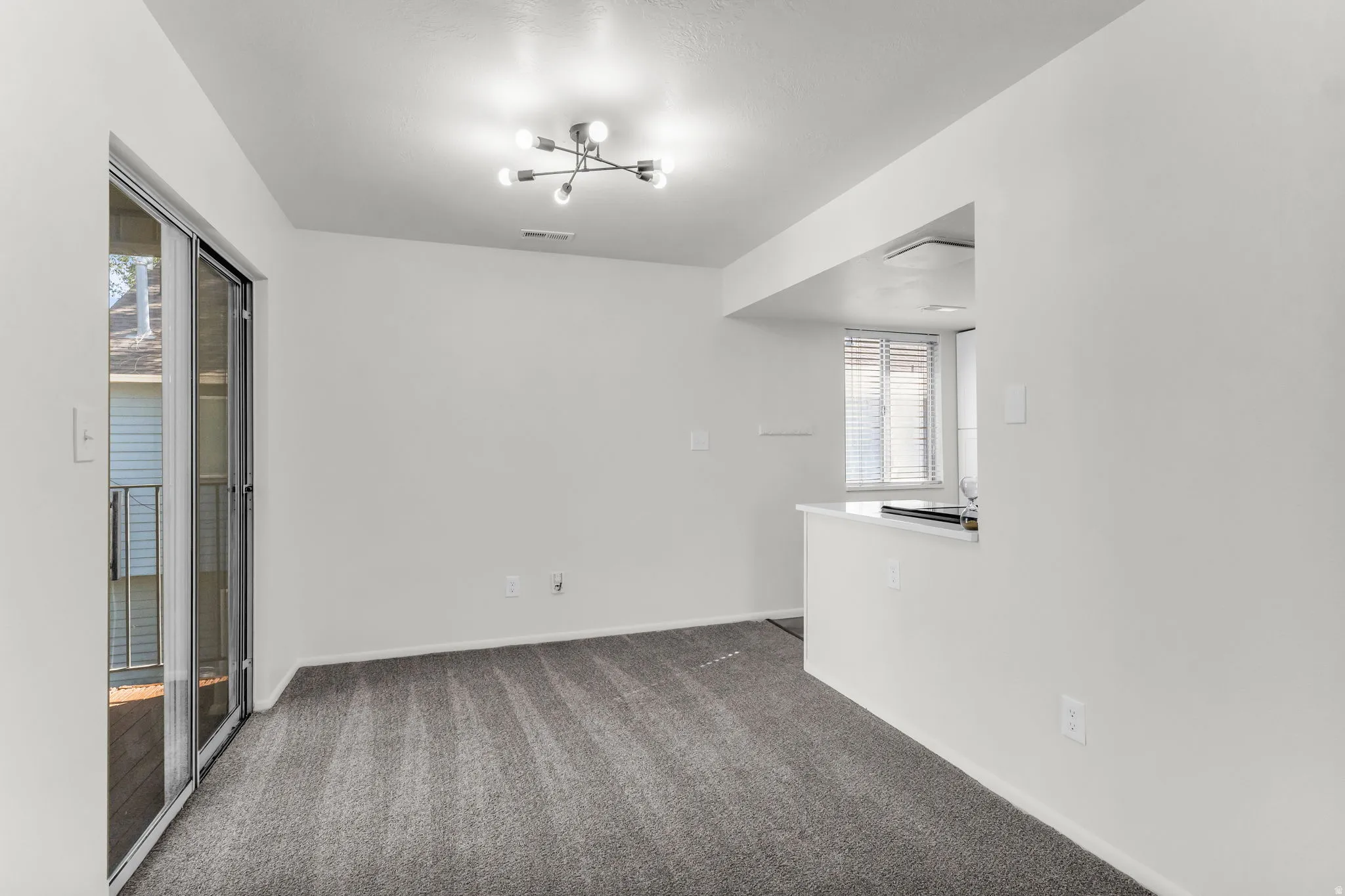 Recessed kitchen pass-through with white countertop, contemporary ceiling light fixture, sliding glass door, and neutral wall paint
