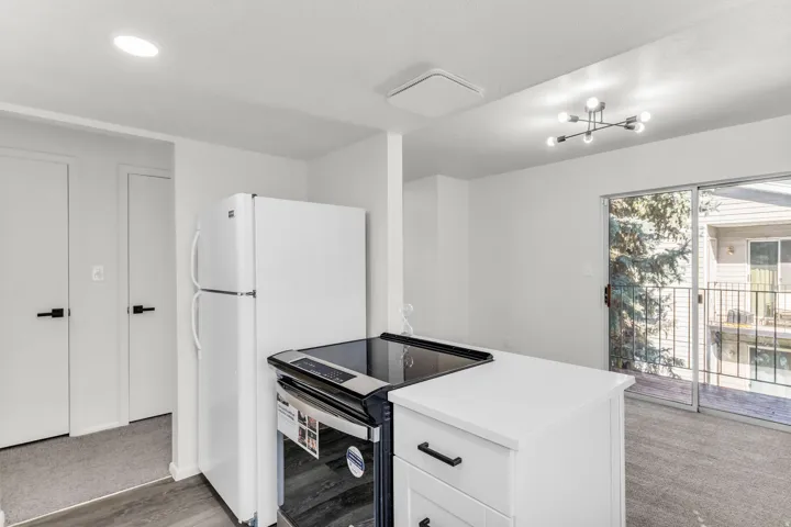 White kitchen cabinetry with matte black hardware, white refrigerator, and a sliding glass door to an exterior balcony
