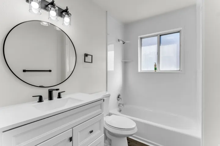 White vanity with matte black fixtures, an oval mirror, and an overhead three-light fixture