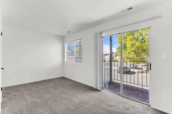 Sliding glass door leading to a balcony with metal railings, a window with blinds, and gray carpet