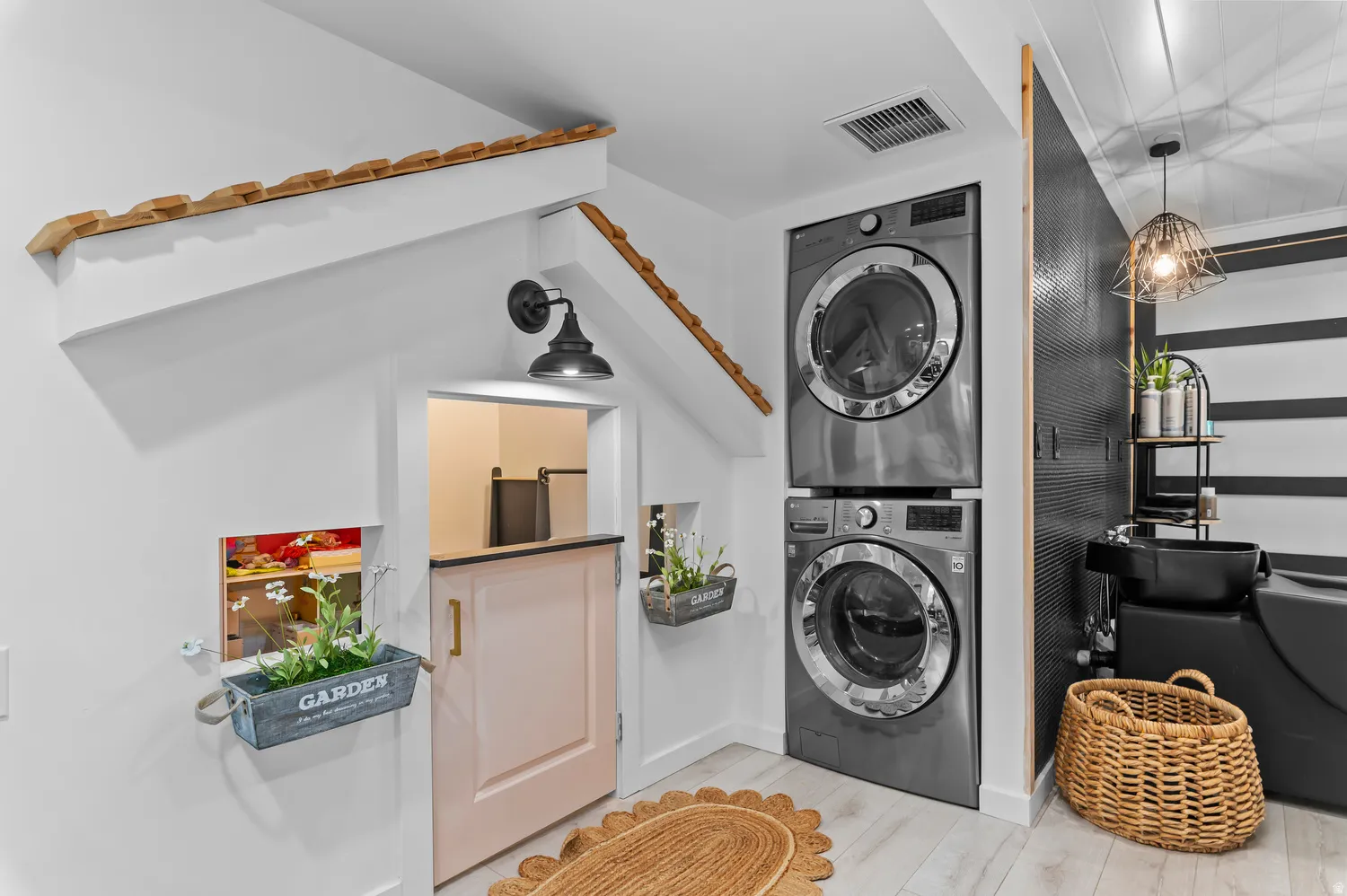 Stacked laundry appliances, light wood-finish flooring, textured accent wall, barn-style door, and decorative wall sconce