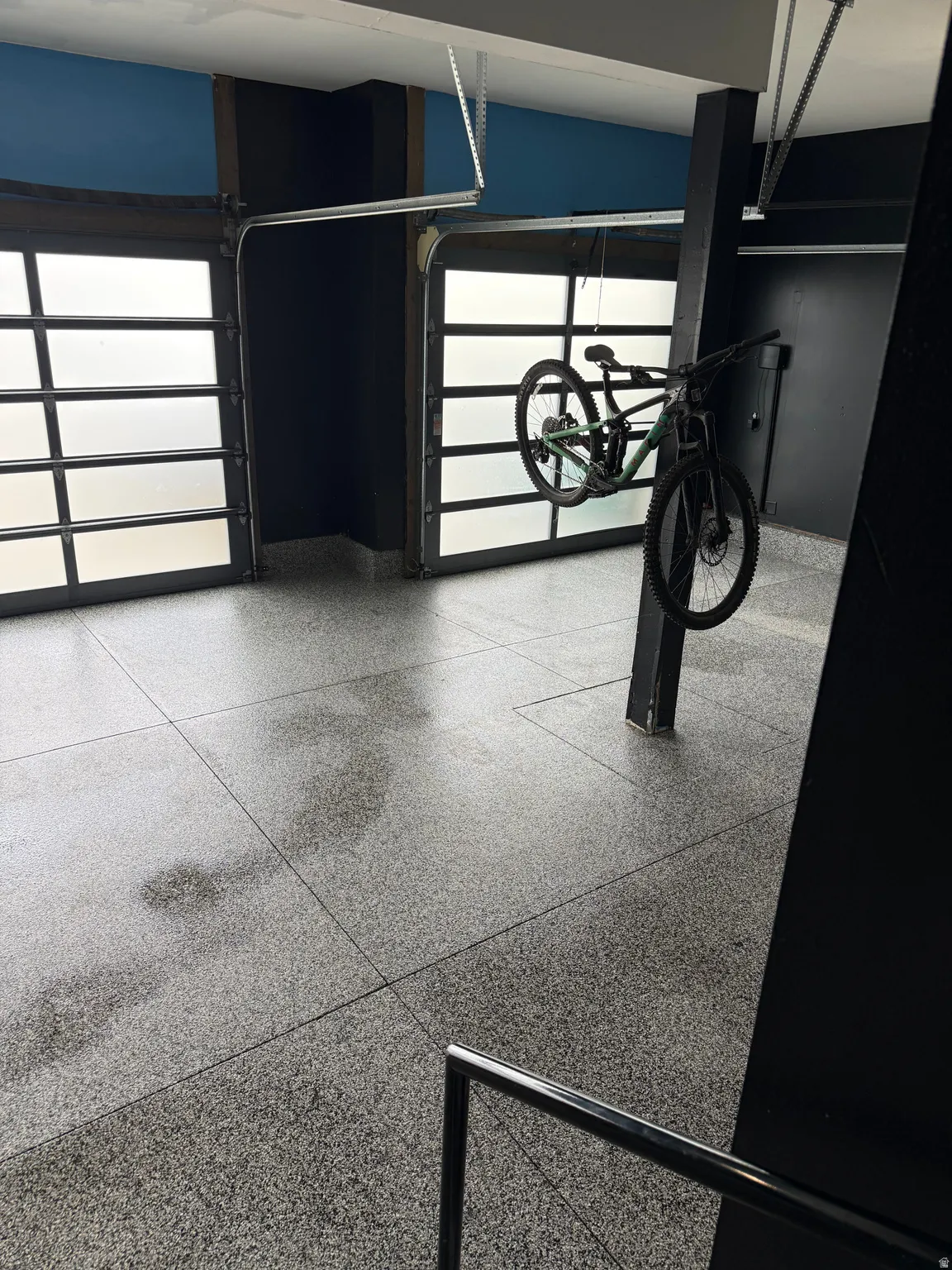 Garage featuring two overhead doors with frosted panels, epoxy-coated flooring, and a metal handrail