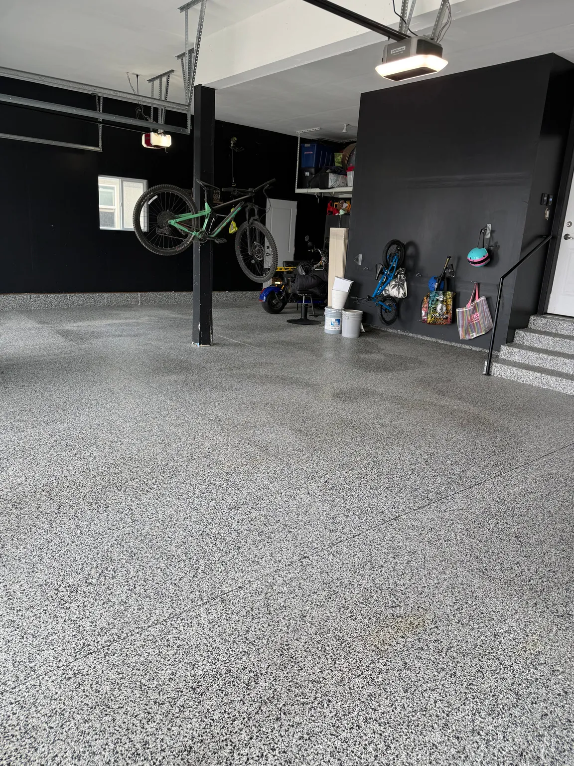 Spacious garage with an epoxy-coated concrete floor, contrasting dark walls, and exposed ceiling joists