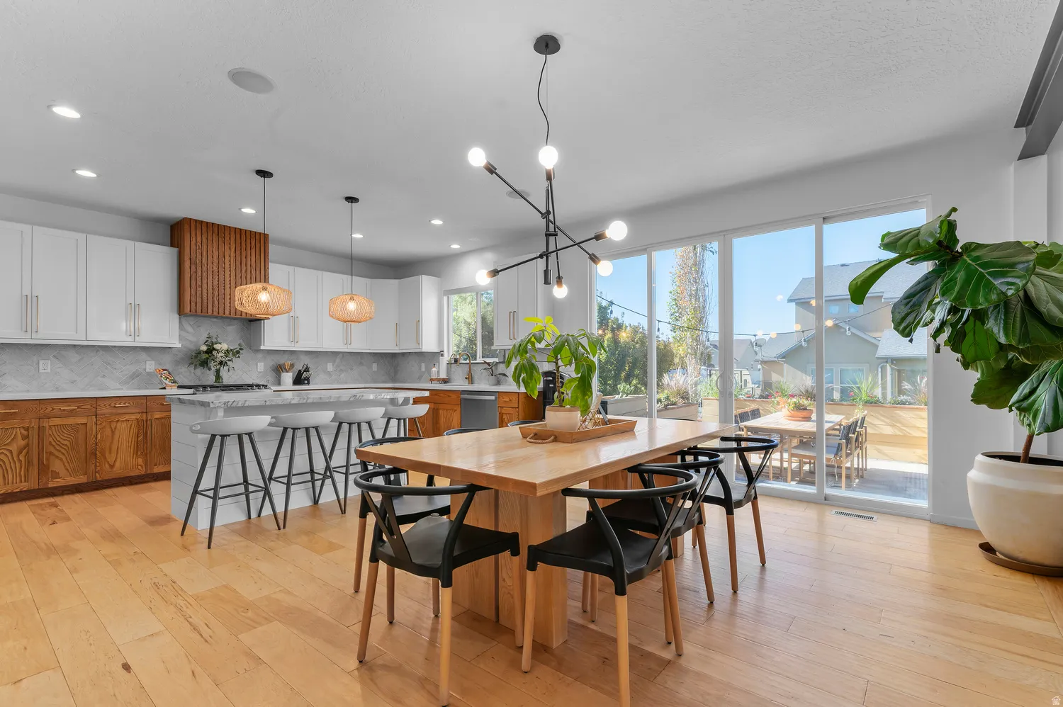 Expansive wood-finish flooring throughout, featuring a kitchen island with seating, white upper cabinetry, and a wood-slat range hood