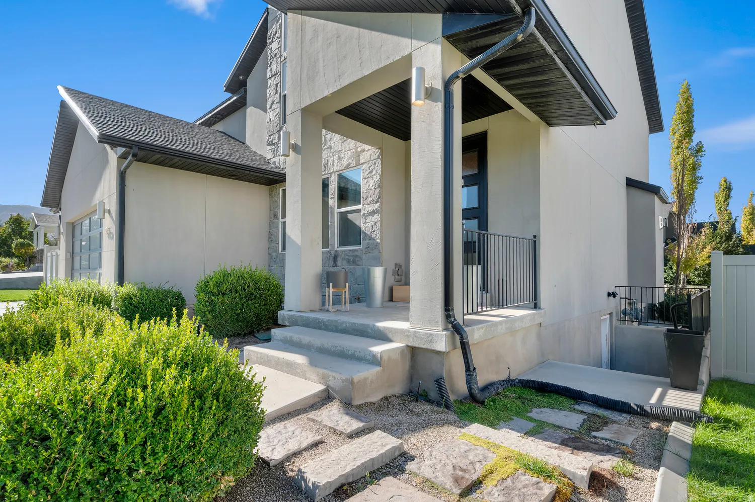 Stucco exterior with stone accents, a covered entry porch, a black metal railing, and a side-entry garage