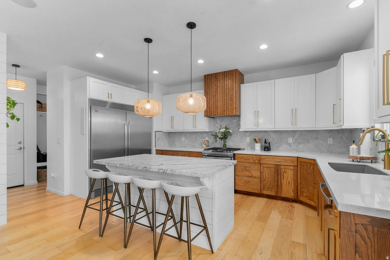 Spacious kitchen featuring an island with a light-toned countertop, stainless steel refrigerator, wood-finish flooring, and pendant lighting