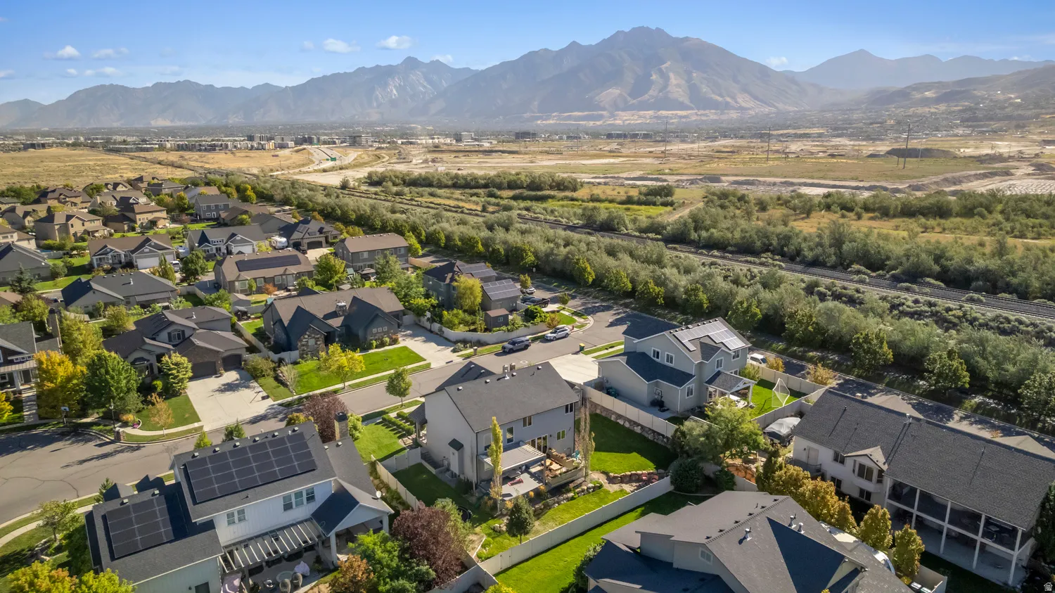 Aerial perspective showcasing a residential area with mature landscaping, mountainous terrain, and a natural riparian area