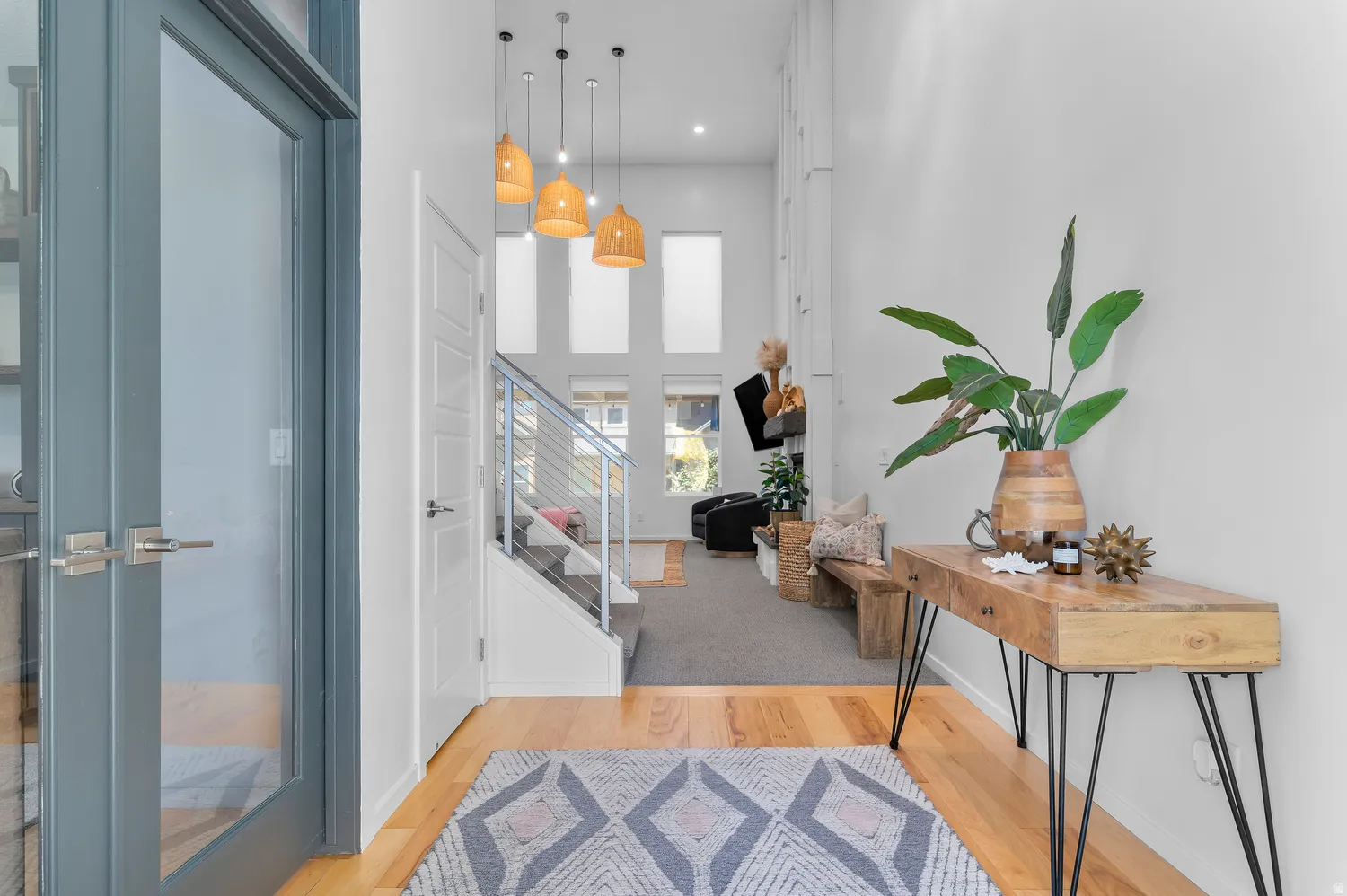 Hardwood flooring, high ceilings, multiple pendant light fixtures, and a staircase with metal railings