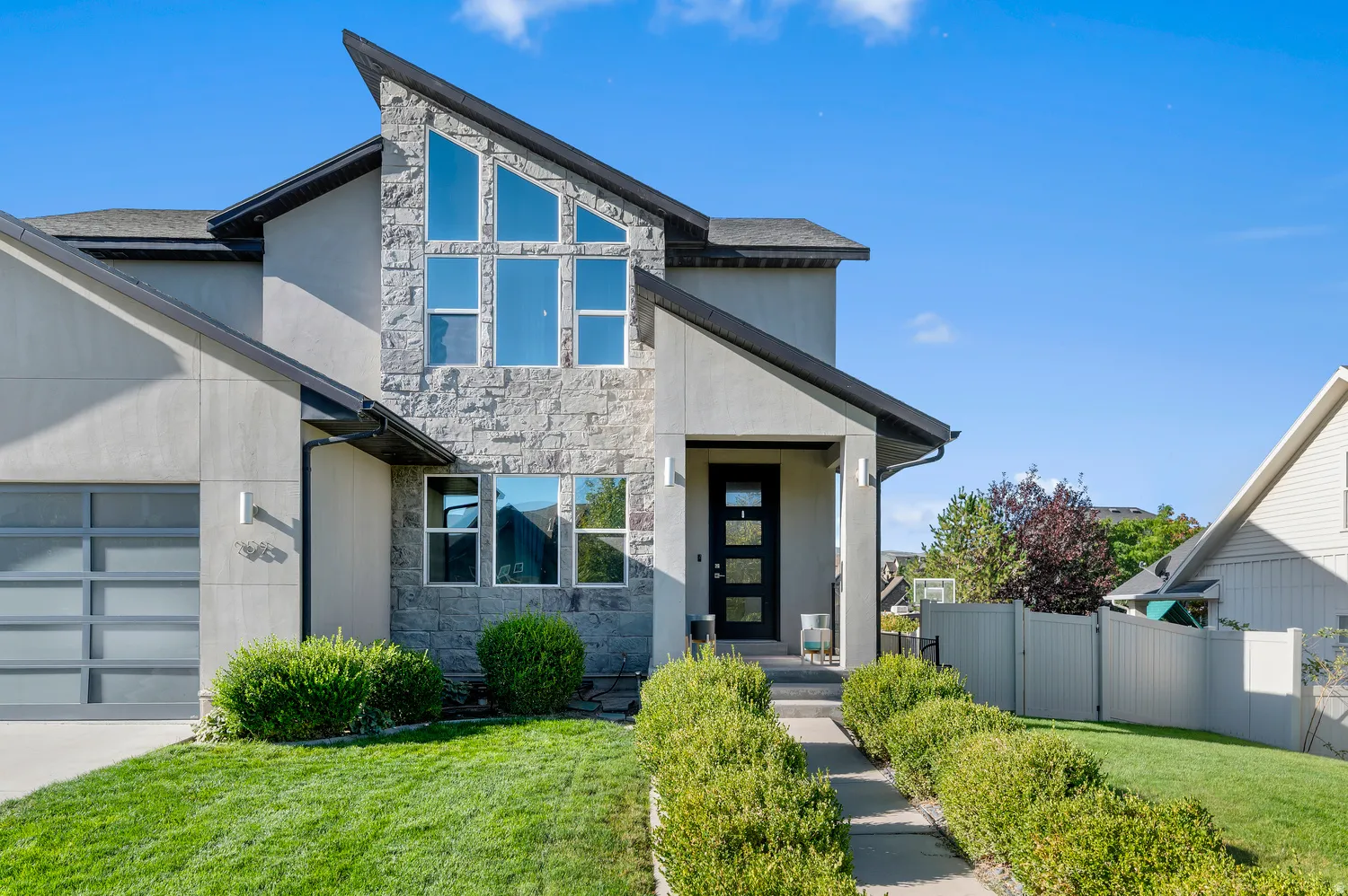 Modern exterior with stone and stucco finishes, a multi-pane front door, and an integrated garage with a frosted panel door