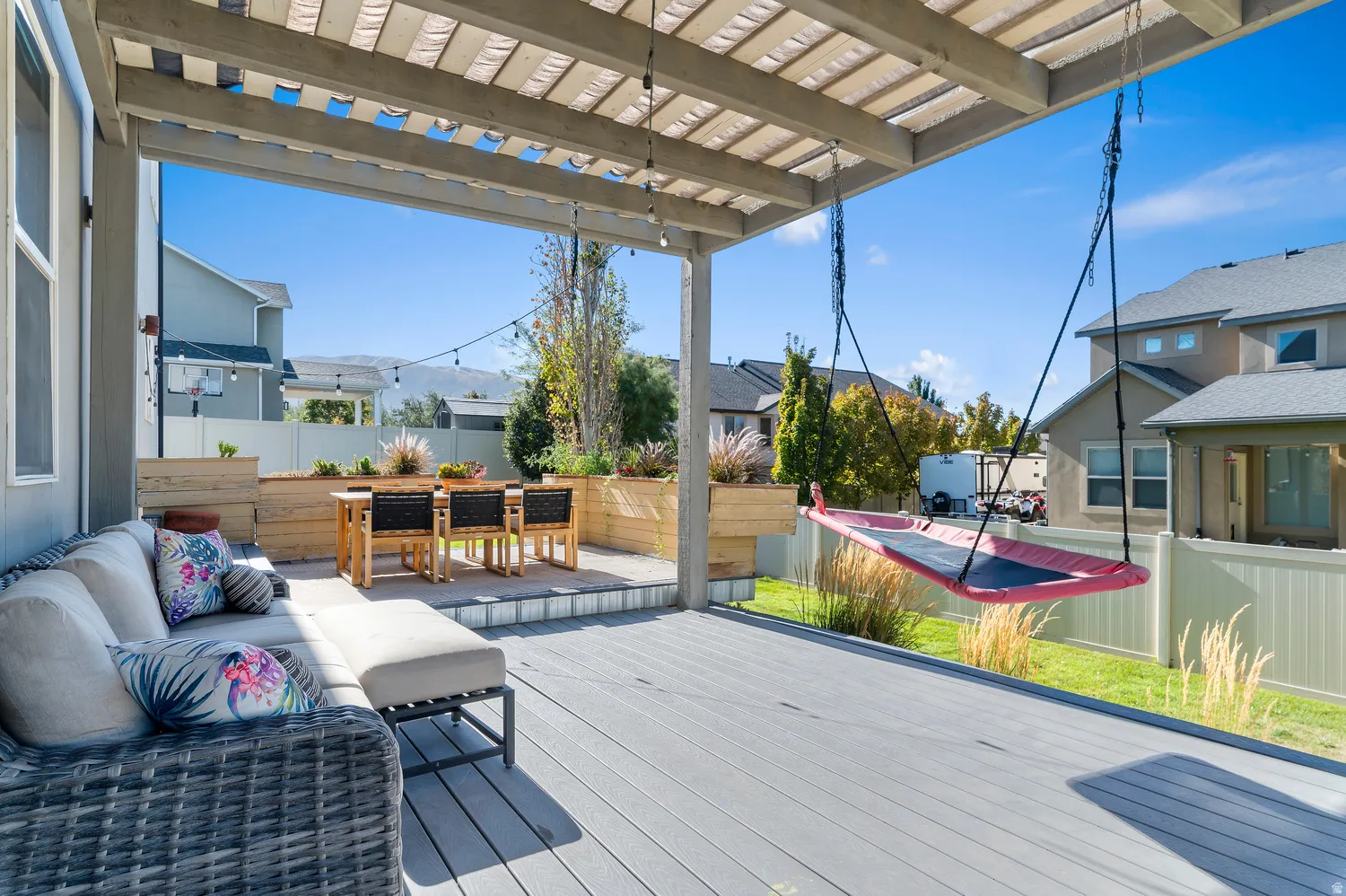 Covered patio featuring a composite deck, slatted pergola, raised garden beds, and an elevated dining area