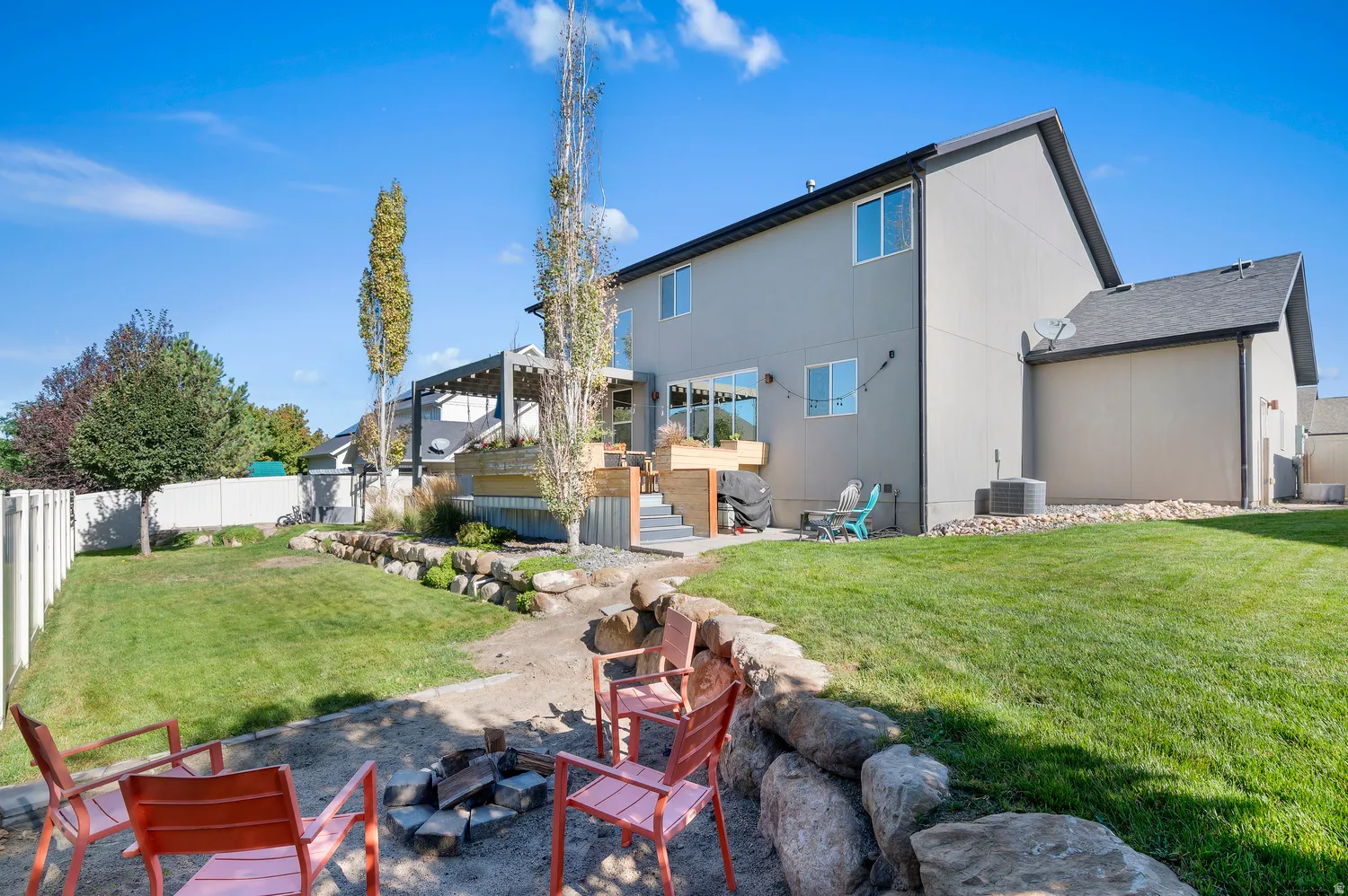 Manicured lawn, tiered deck with pergola, rock retaining wall, and a fire pit area