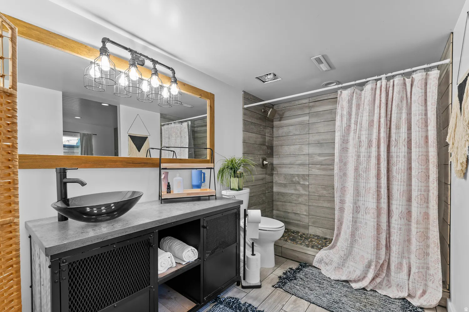 Black vessel sink with a matte black faucet, industrial-style vanity with mesh cabinet fronts, wood-framed mirror, and a five-light vanity fixture