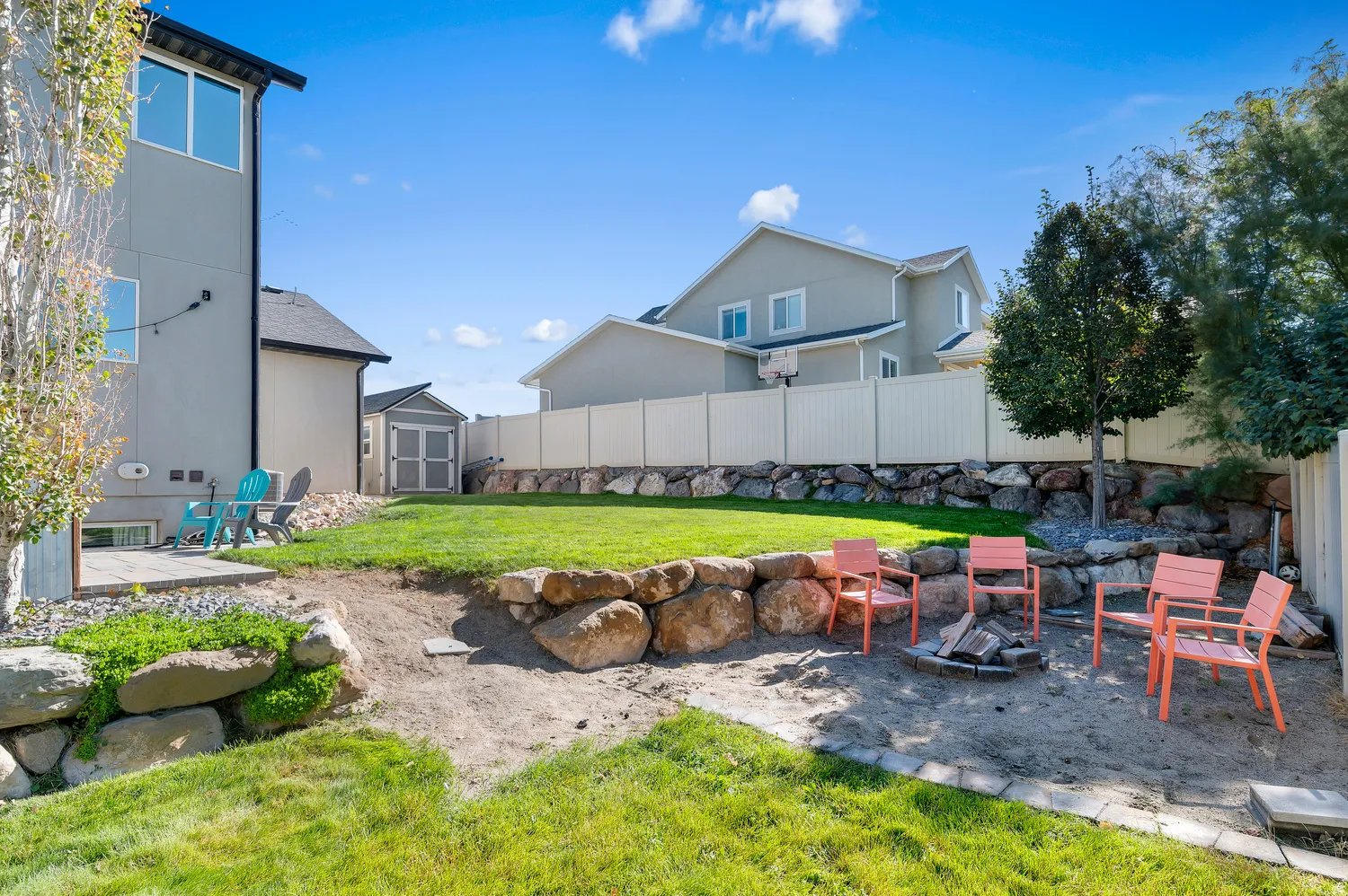 Tiered backyard featuring a manicured lawn, a gravel patio with a built-in fire pit, stone retaining walls, and a separate storage shed