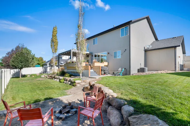 Manicured lawn, tiered deck with pergola, rock retaining wall, and a fire pit area