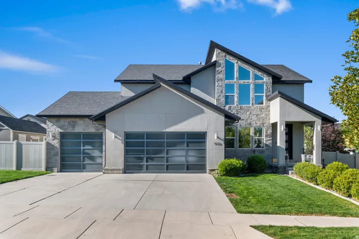 Modern exterior with a stone and stucco finish, featuring an angular roofline, a prominent window array, and two garage bays with frosted glass doors