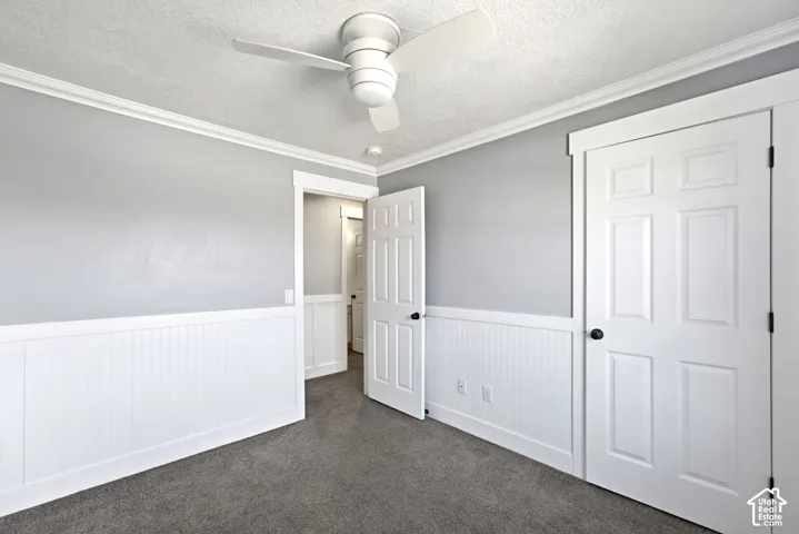 Grey carpeted flooring, white beadboard wainscoting, white crown molding, white paneled doors, and a ceiling fan