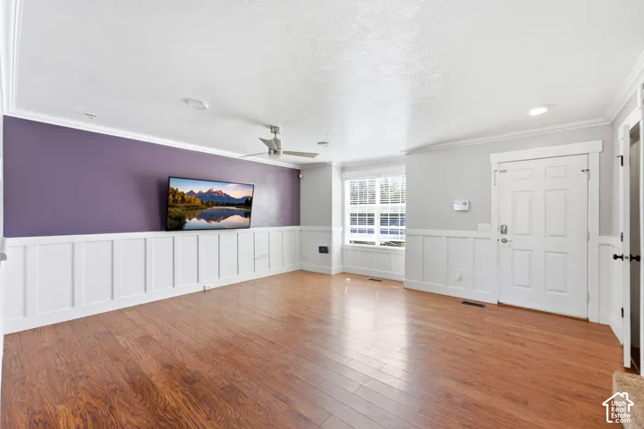 Wood-finish flooring, white wainscoting, ceiling fan, recessed lighting, and a multi-pane window