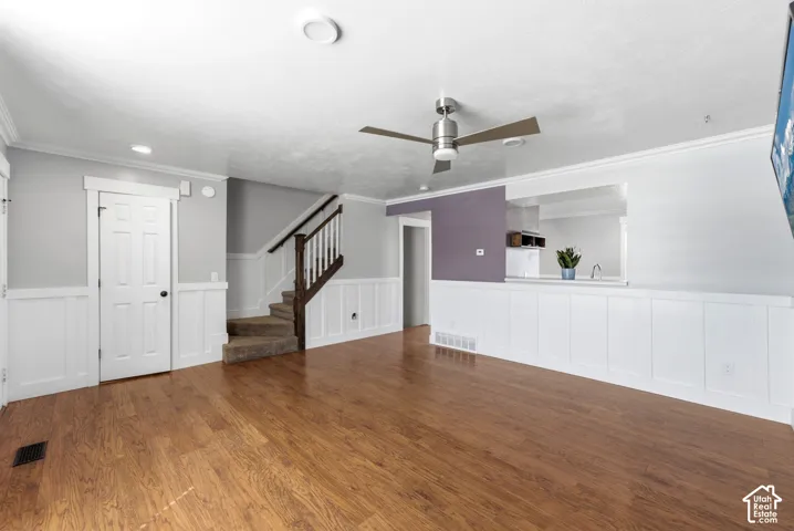 Wood-finish flooring, white wainscoting, contemporary ceiling fan, built-in counter with sink, and carpeted stairs with wood banister