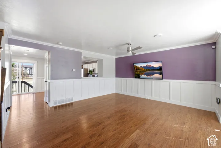 Wood-finish flooring, white wainscoting, crown molding, ceiling fan, and recessed lighting
