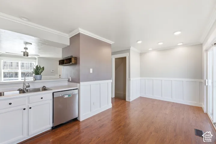 Recessed lighting with crown molding, stainless steel dishwasher, white cabinetry with dark hardware, wood-finish flooring, and white paneled wainscoting