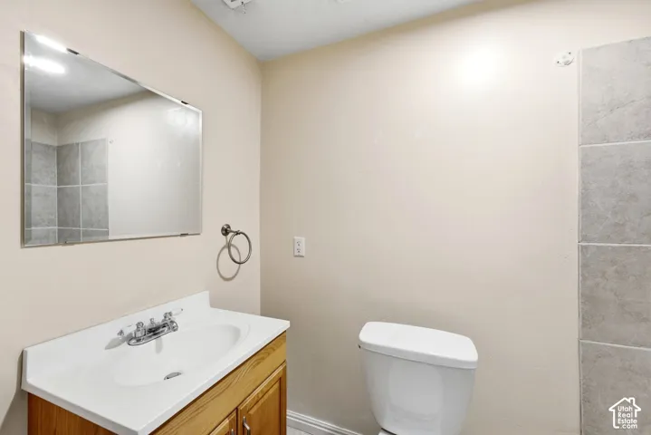 Bathroom featuring a wood-finish vanity with an integrated sink, a wall-mounted mirror, and tile shower surround