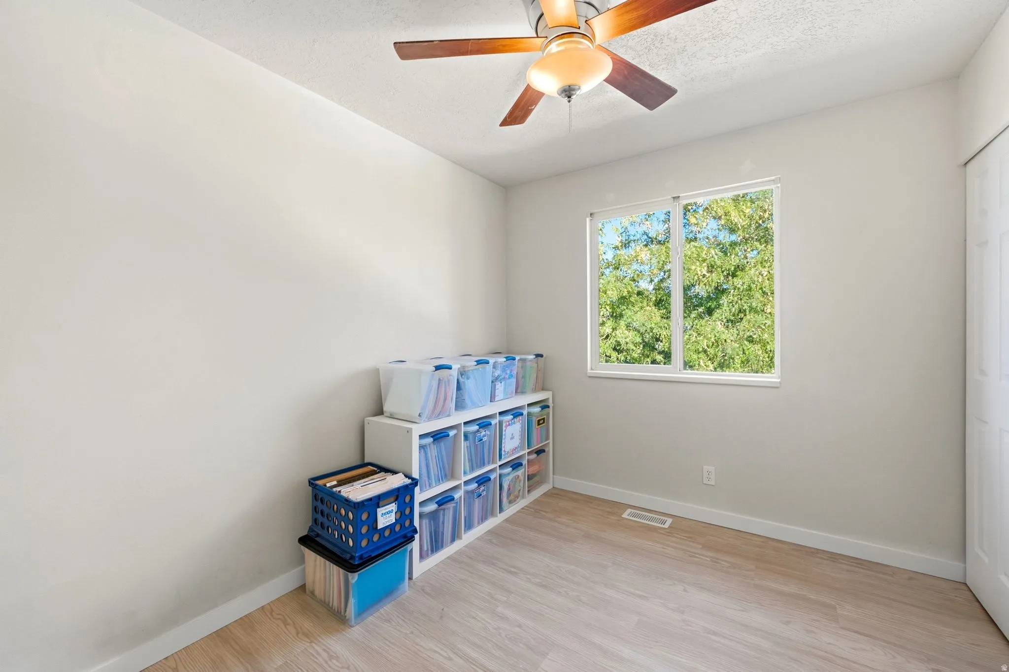 Neutral wall paint, wood-finish flooring, white trim, and a ceiling fan with integrated lighting