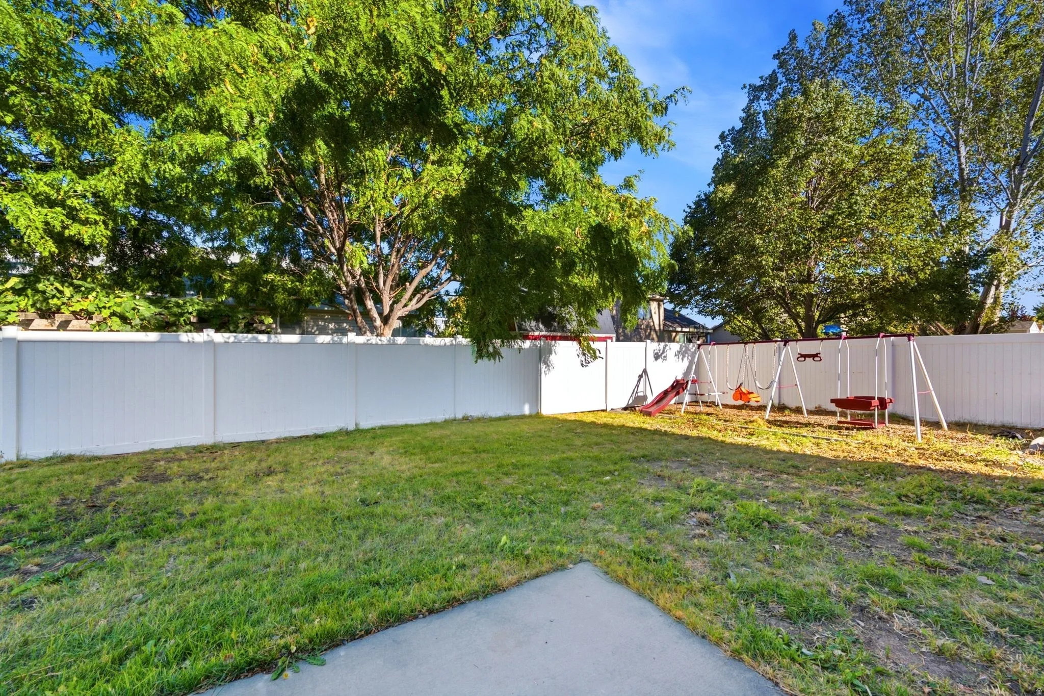 Expansive backyard featuring a manicured lawn, perimeter fencing, mature trees, and a concrete pad