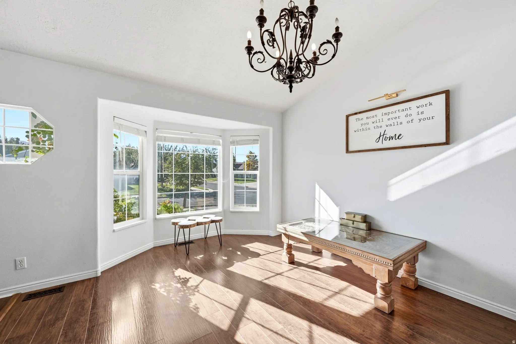Vaulted ceiling with an ornamental chandelier, bay windows, wood-finish flooring, and white walls