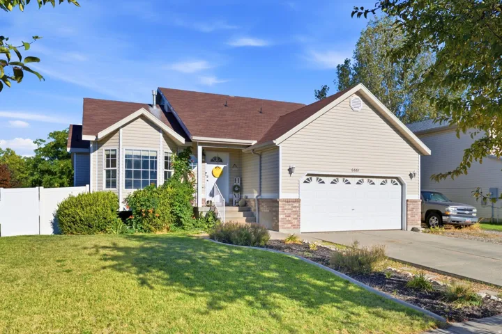 Two-story residence featuring light-colored siding, a brown shingled roof, a front-facing garage with an overhead door, a concrete driveway, and a front lawn with foundational shrubs
