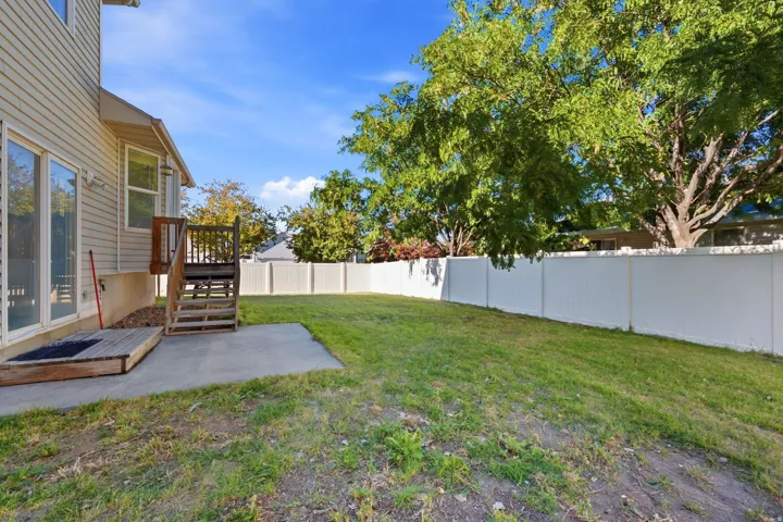 Expansive backyard with a manicured lawn, white privacy fencing, and mature trees