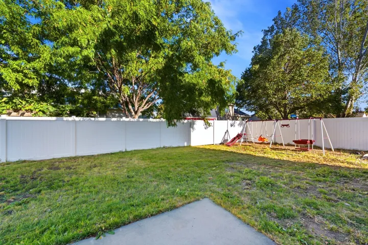 Expansive backyard featuring a manicured lawn, perimeter fencing, mature trees, and a concrete pad