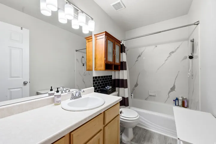 Recessed lighting, wood-finish cabinetry, white solid surface countertop, white ceramic sink, and a full wall mirror