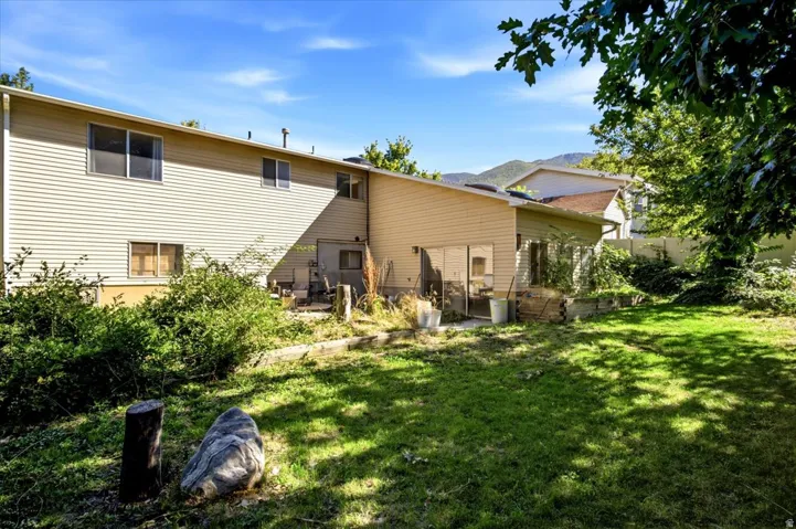 Expansive rear yard with a grass lawn, mature trees, and a mountain backdrop