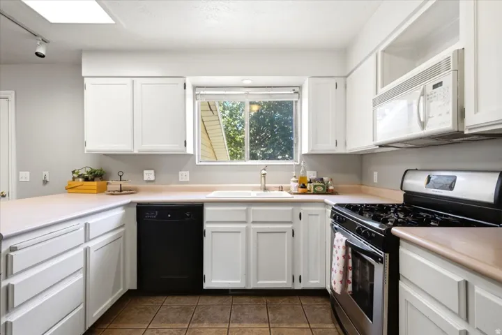 Kitchen featuring white cabinetry, a built-in microwave, a gas range, a white sink, and tile flooring