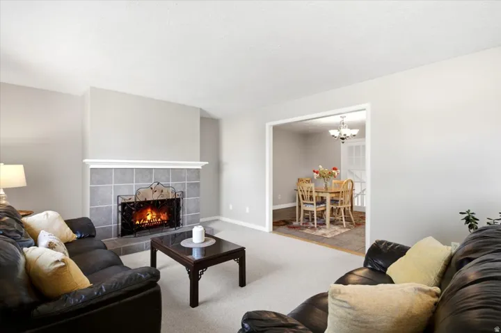 Living area featuring a tiled fireplace with mantel, framed opening to a dining space, and wall-to-wall carpeting